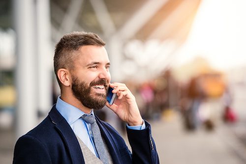 Biznesmen rozmawiający przez telefon przed terminalem lotniska | Podróże służbowe z LOT