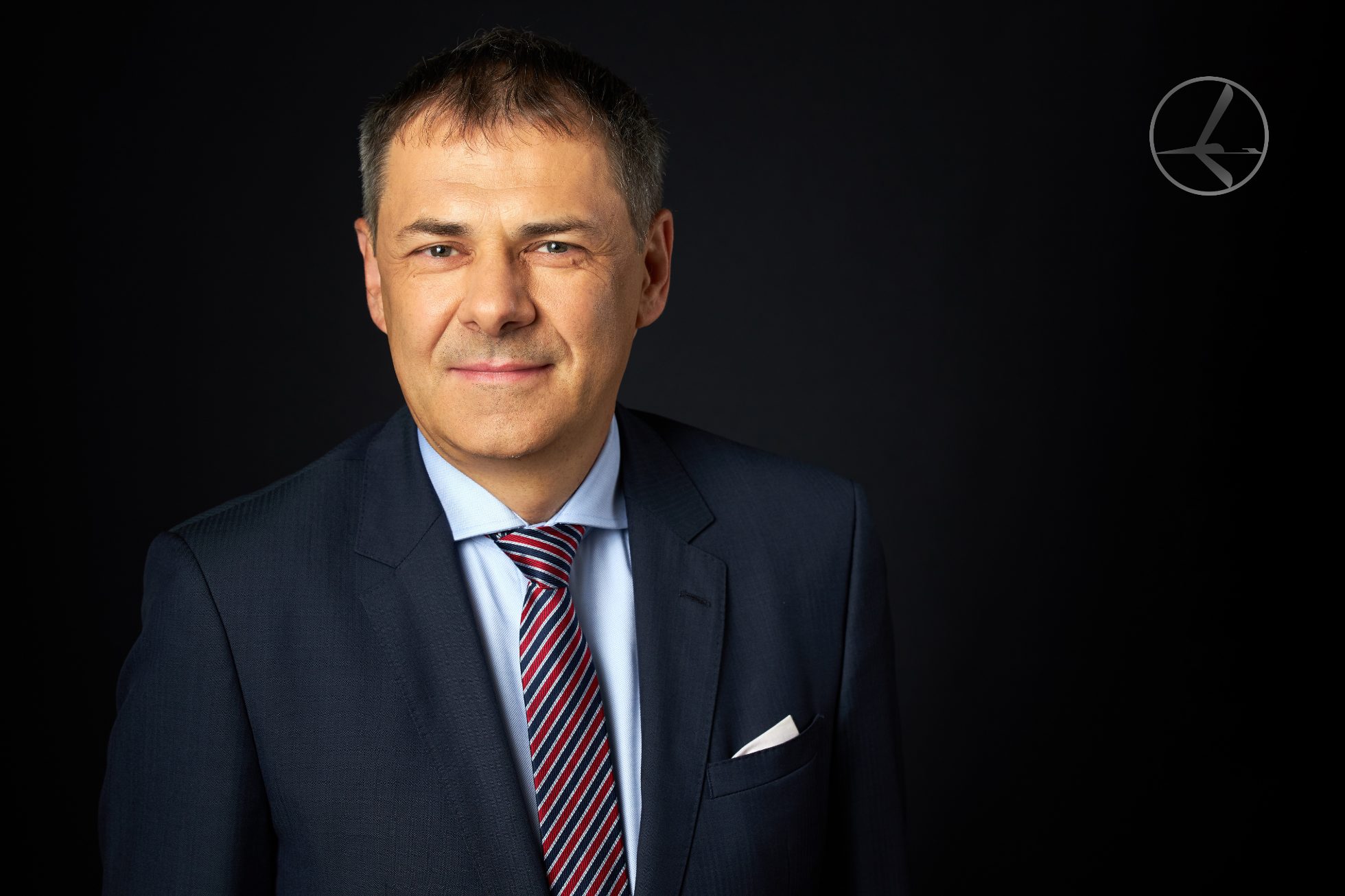 Mężczyzna w garniturze siedzi na krześle i patrzy w kamerę.