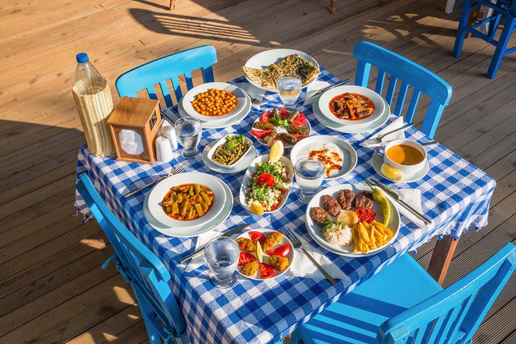 Na obrazku widoczne są greckie przekąski (meze) na białym tle. Zestaw zawiera oliwki, ser feta, oliwki, pomidory, ogórki i pieczywo.