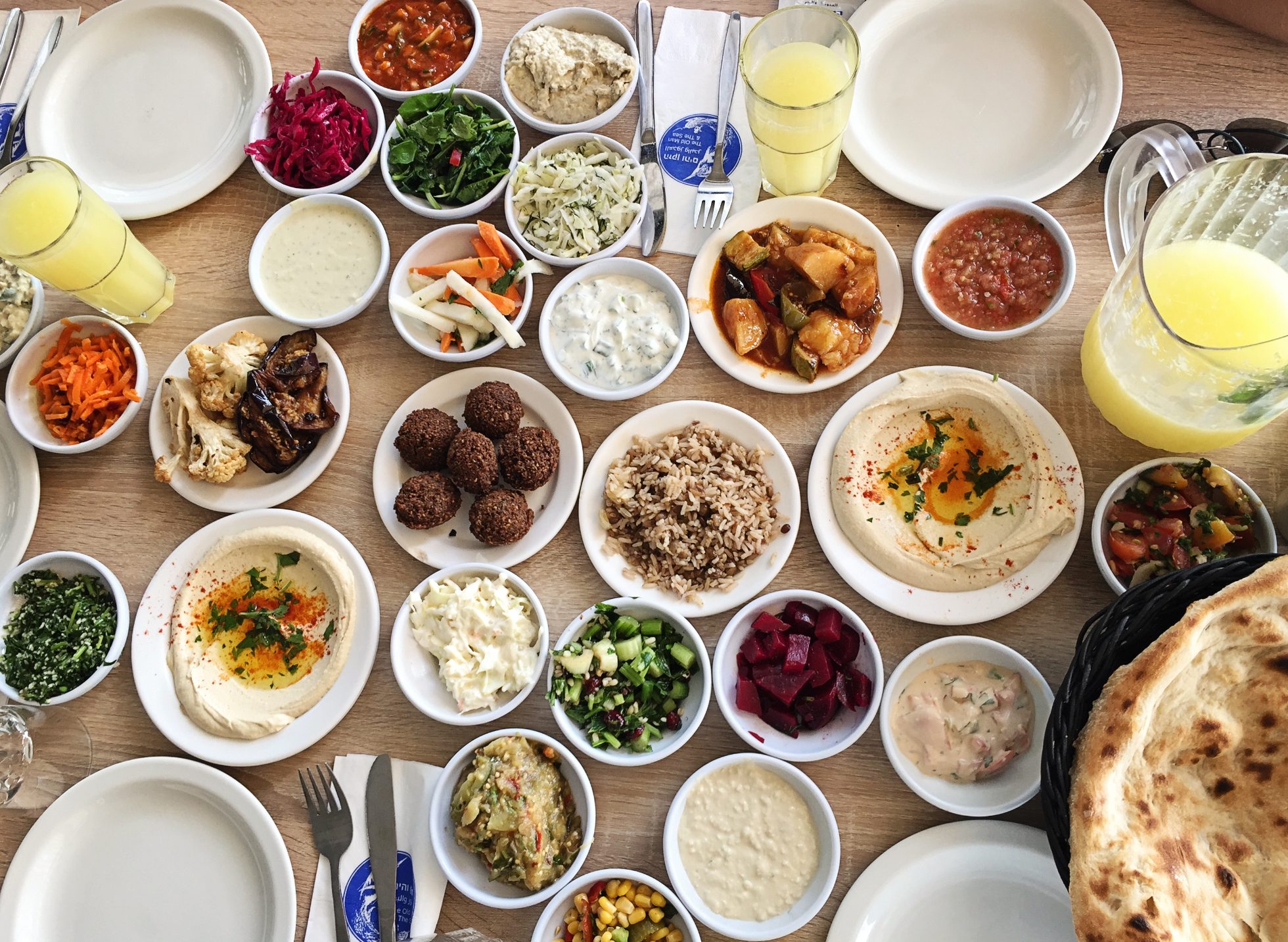 Stół z izraelskimi przekąskami - hummus, falafel, tahini, sałatki, guacamole, kuskus, chleb pita, tabbouleh, tzatziki, ryż, feta, meze, kapusta, bakłażan, kukurydza, marchew, cukinia. Świeże soki., kuchnia Izraela