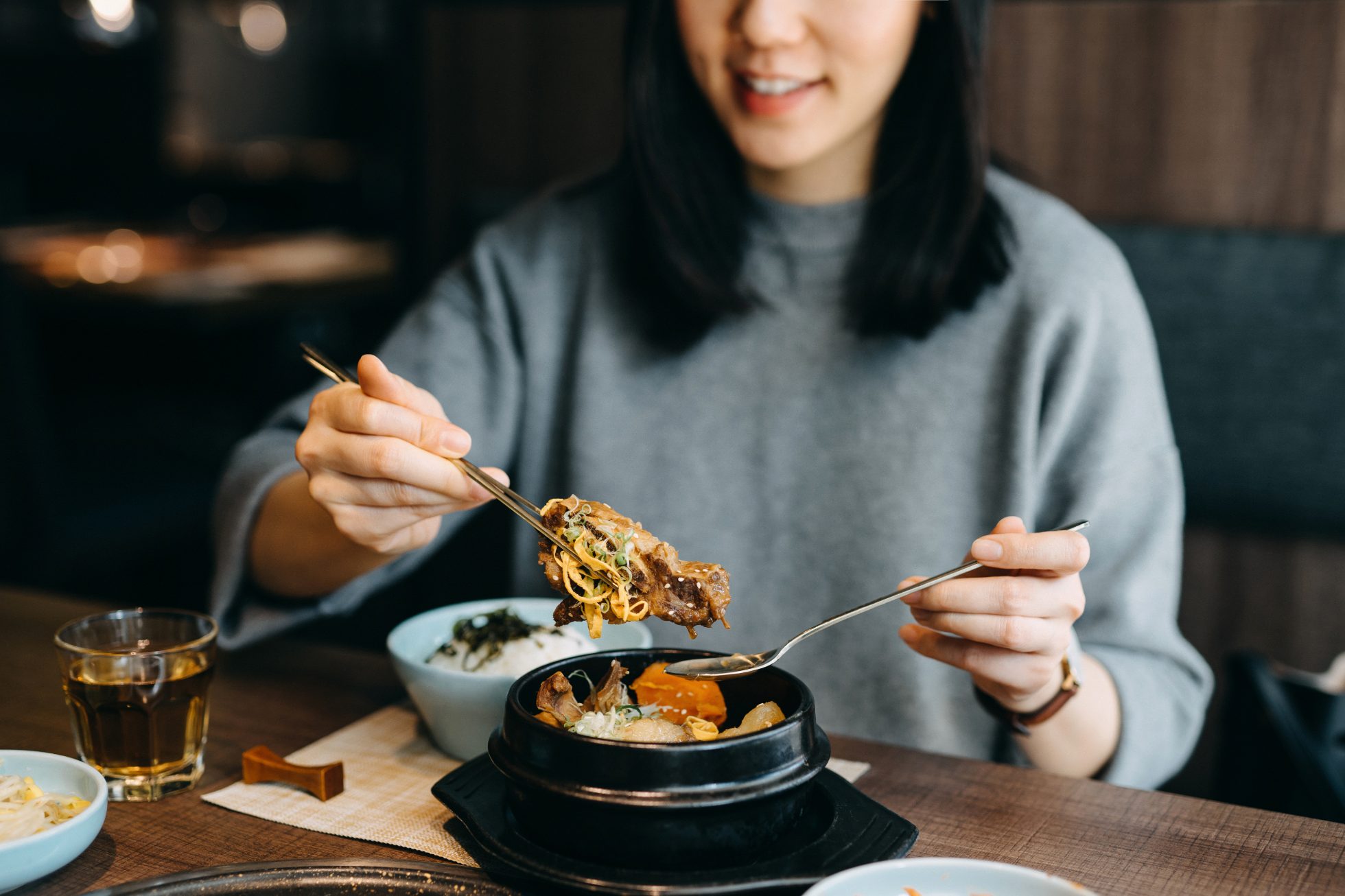 uśmiechająca się azjatka je ze smakiem koreańskie danie w koreańskiej knajpce, kuchnia koreańska