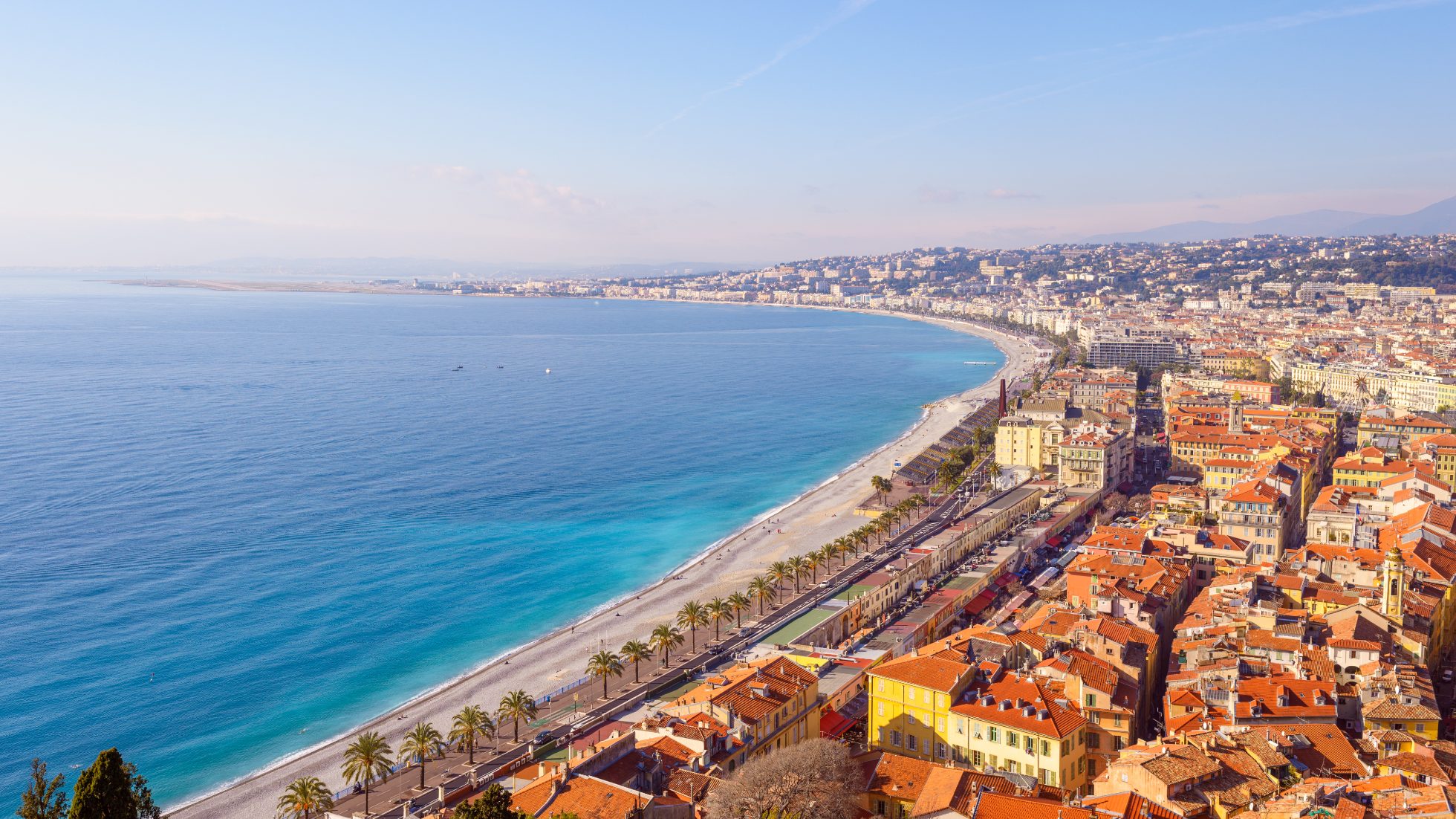 Panoramiczny widok na miasto Nicea, jego promenadę i plażę, turkusowe morze, w piękny słoneczny zimowy dzień. Stolica departamentu Alpes-Maritimes położona jest na wybrzeżu Morza Śródziemnego, na Lazurowym Wybrzeżu, na południu Francji. Na pierwszym planie stare miasto i w oddali lotnisko Nice Cote d'Azur.