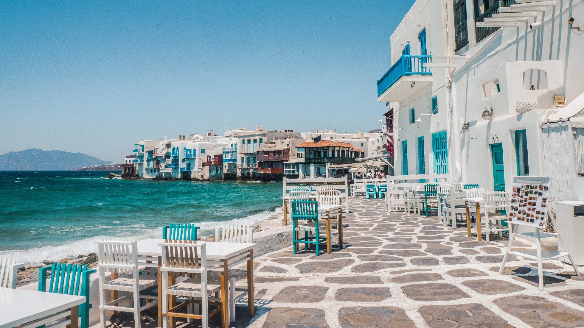 Wybrzeże Mykonos - białe budynki nad morzem o zachodzie słońca. Wyspy w Grecji.