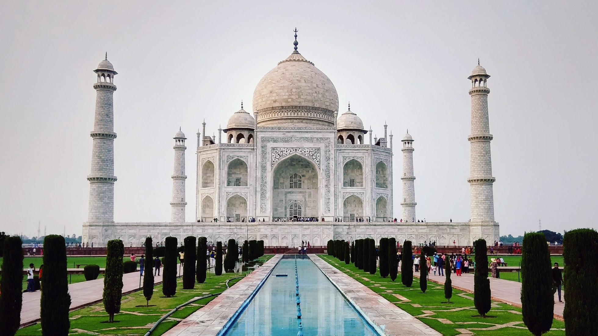 Widok na mauzoleum Taj Mahal w Indiach przy wodzie otoczonej cyprysami.