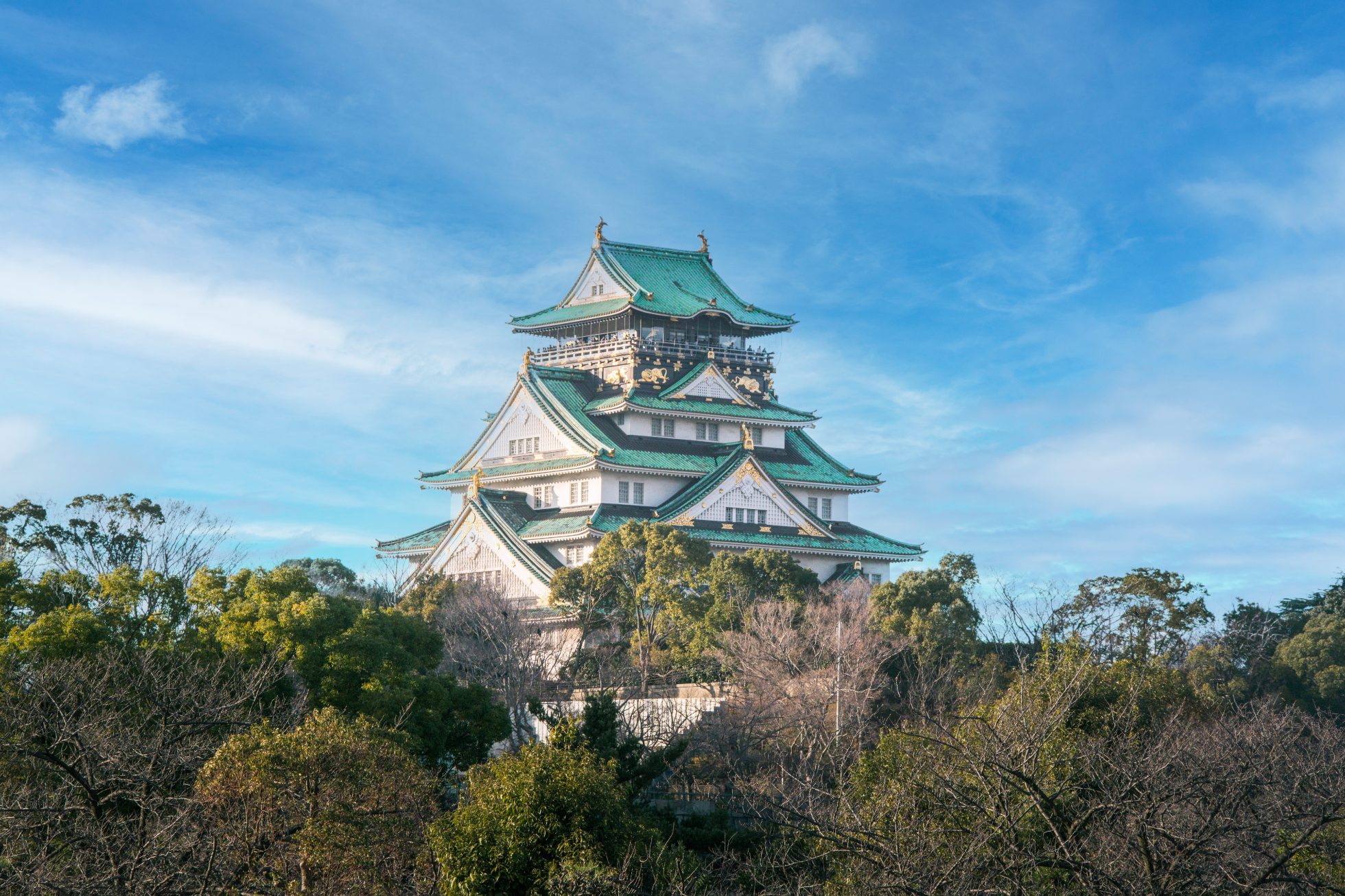 Zdjęcie przedstawia zamek w Osace, Japonia. Budowla jest otoczona wodą, a w tle widać niebieskie niebo.