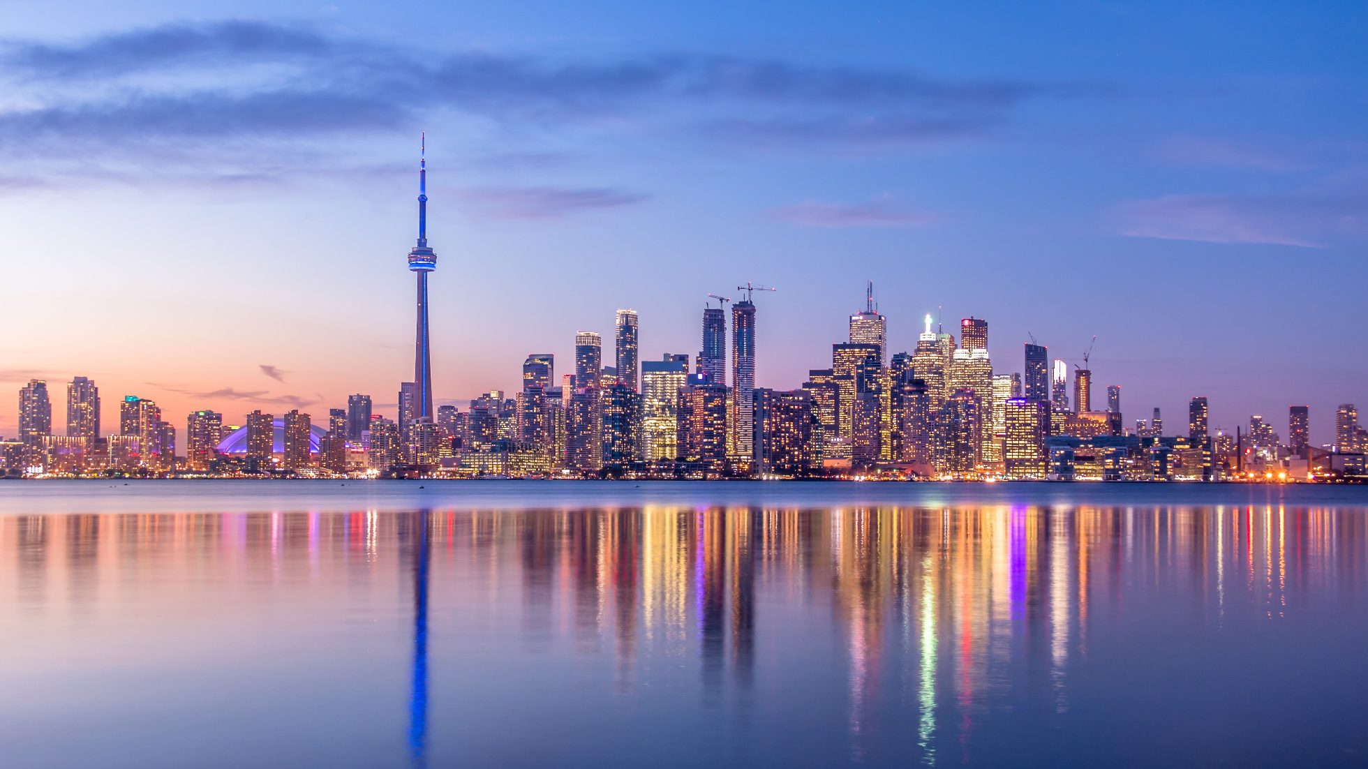 A view of Toronto's skyline from Lake Ontario, featuring the CN Tower and skyscrapers at sunset.
