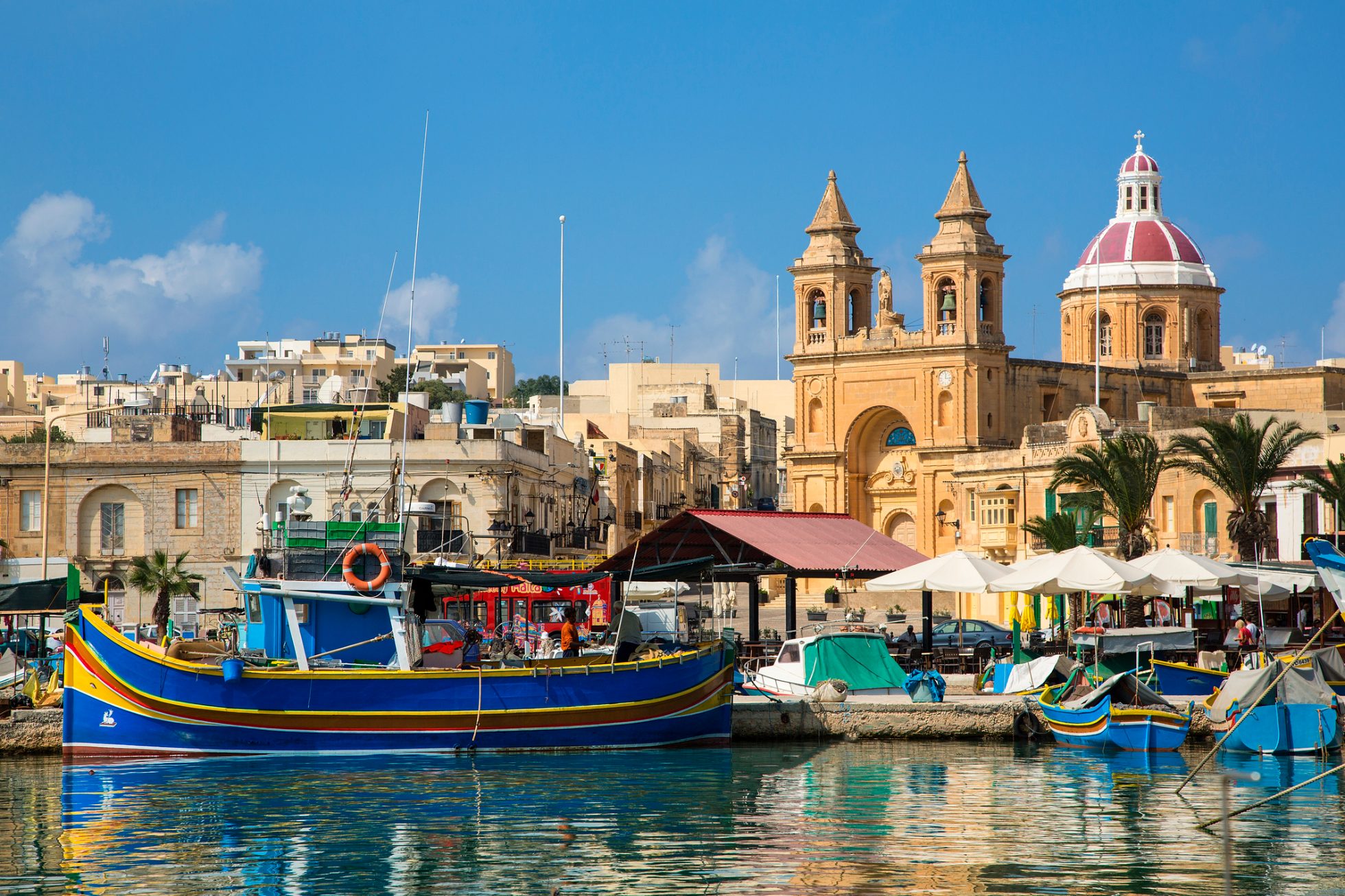 Malta, Marsaxlokk, port wioski rybackiej na południowym wybrzeżu z kolorowymi łodziami rybackimi Kajjiki i kościołem pod wezwaniem Matki Bożej Różańcowej Madonny z Pompei.