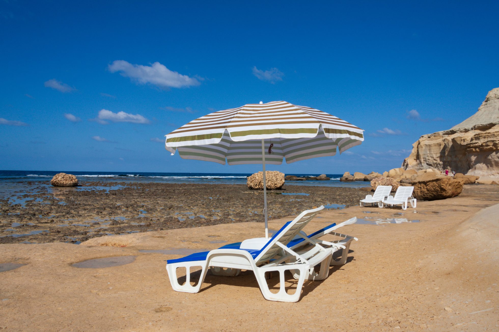 Dwa leżaki i parasol plażowy obok brzegu zatoki Xwejni na Gozo.