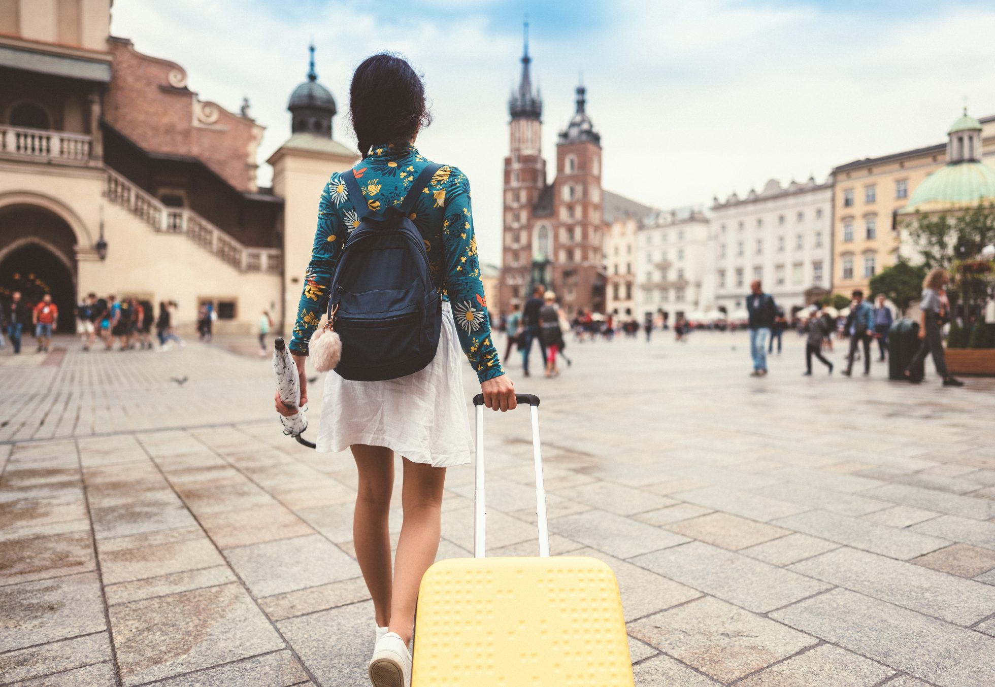 Widok z tyłu kobiety z walizką i parasolką przenoszącej się do Krakowa