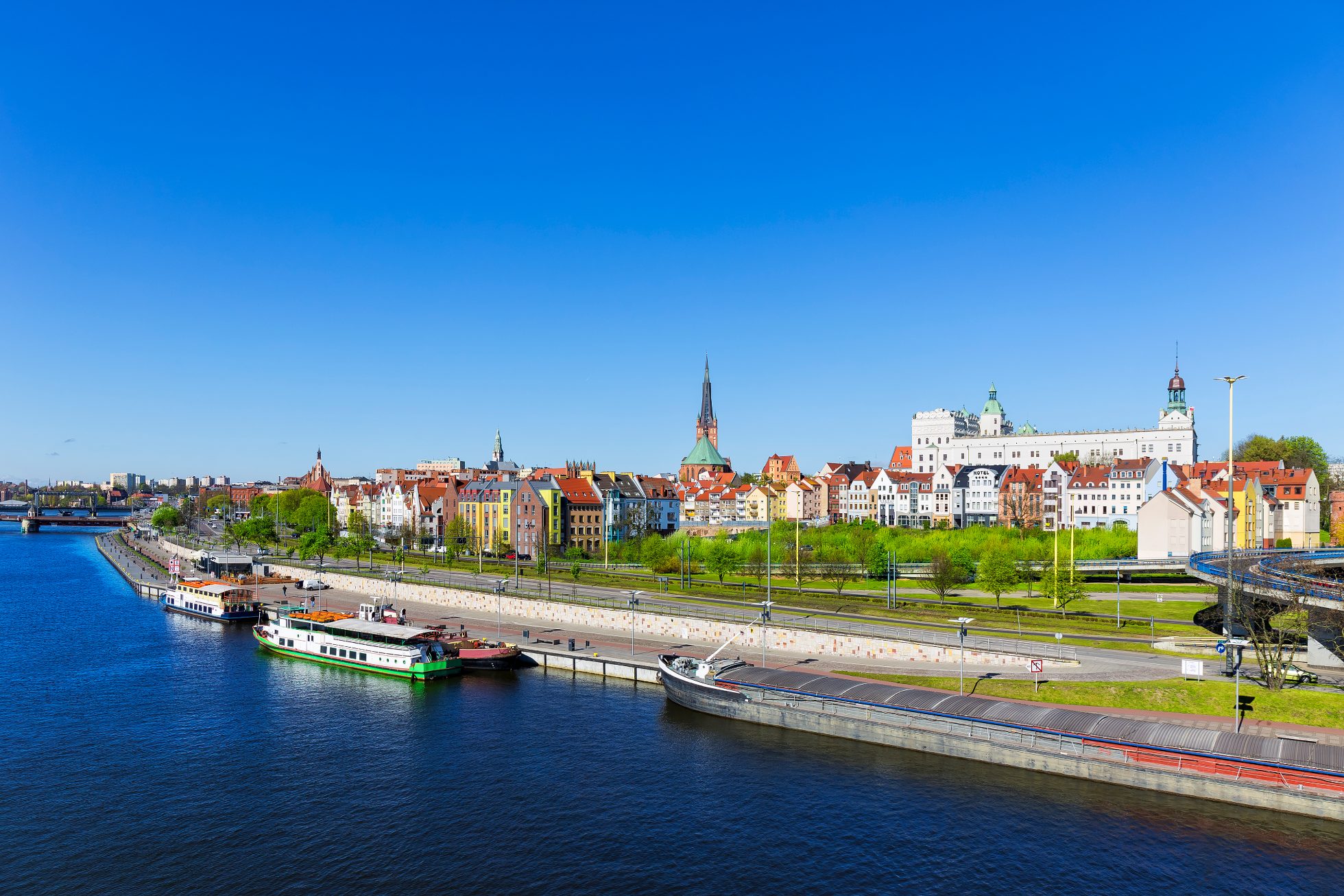 Duży bark rzeczny i statki wycieczkowe przycumowane do nabrzeża na rzece Odrze, Stare Miasto Szczecina w tle