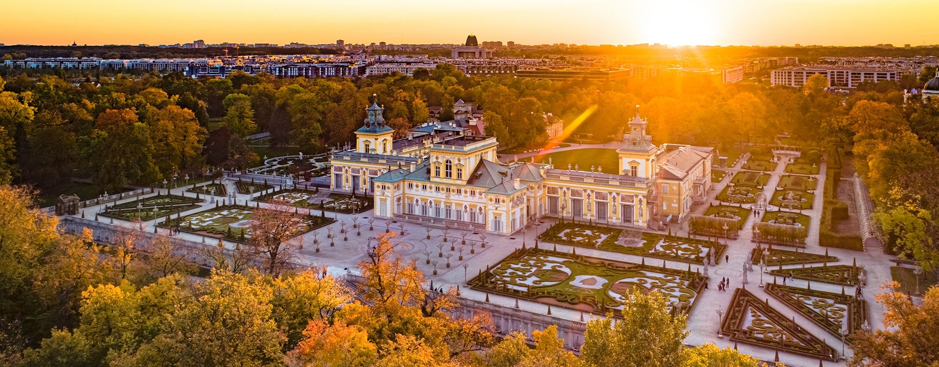 Zdjęcie przedstawia zamek w stylu barokowym z zielonymi ogrodami wokół.