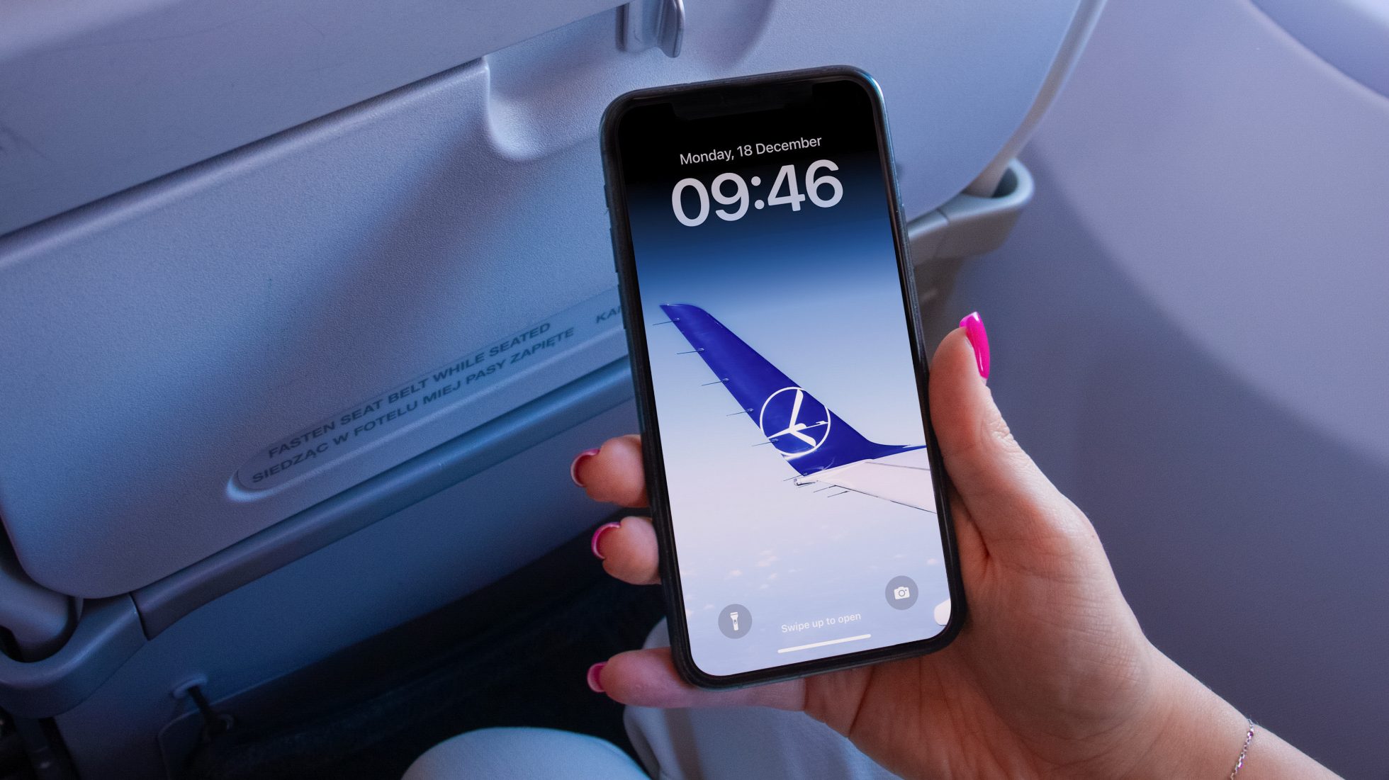 dłoń kobiety trzymająca telefon z tapetą LOT-u na telefon (skrzydło Embraera)