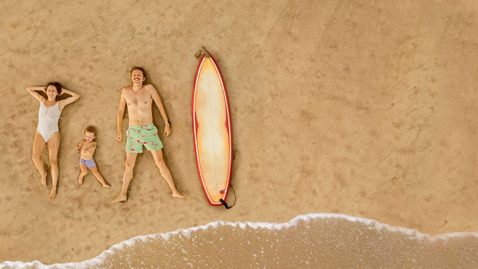Rodzina z małym dzieckiem oplająca się na plaży z deską surfingową obok nich