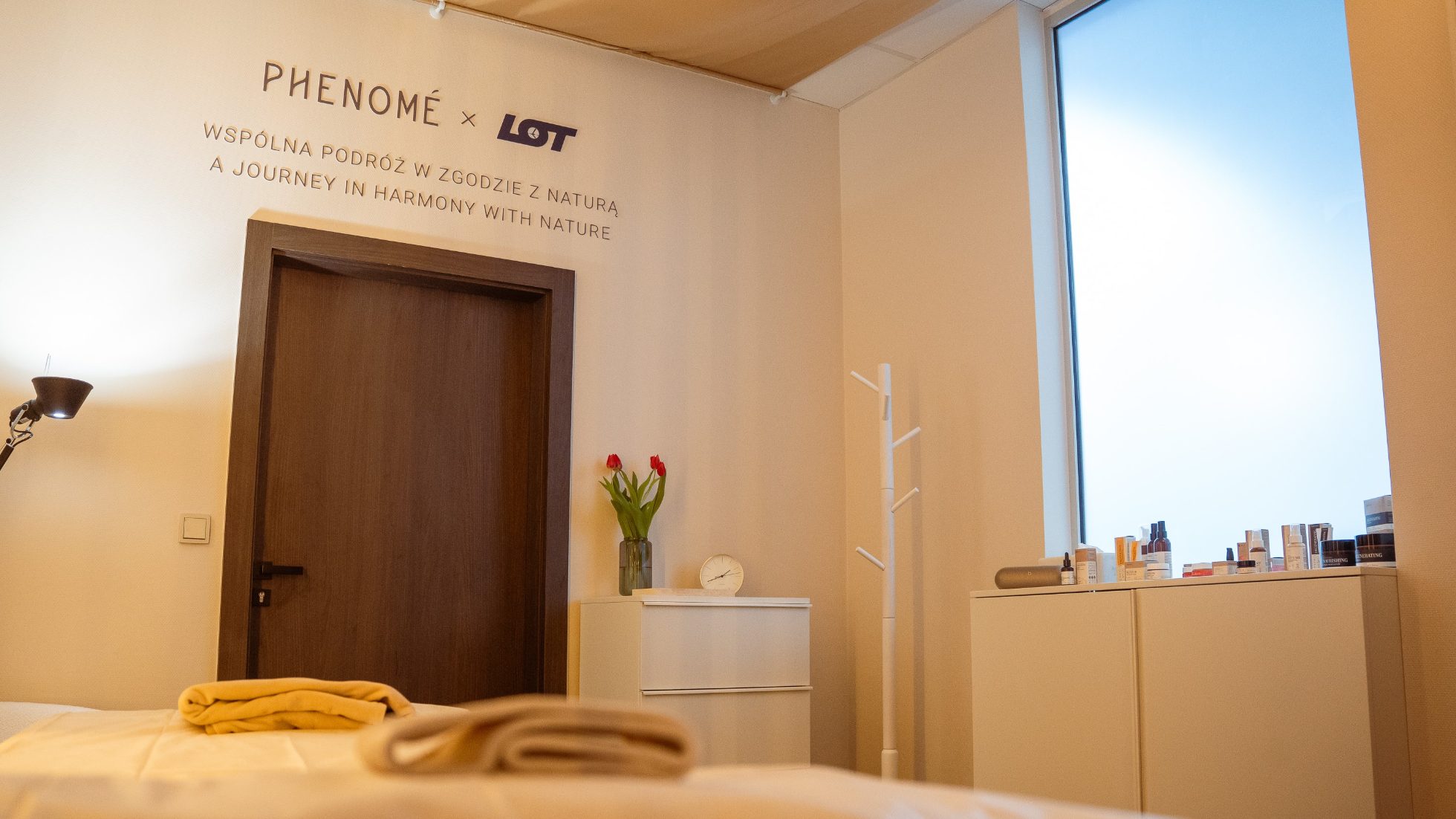Strefa spa Phenome w LOT Business Lounge Polonez - drzwi, biały cabinet z kwiatami oraz tabliczki LOT i Phenome.