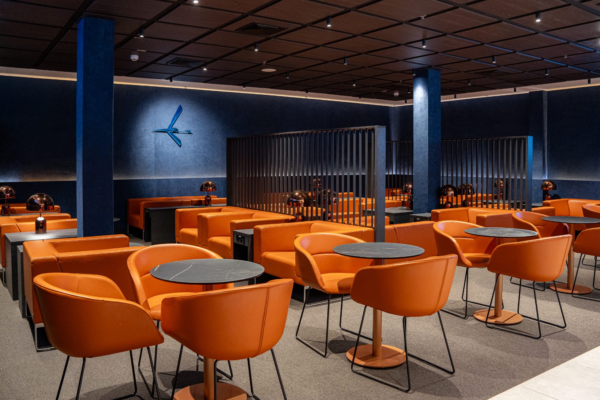 Polonez Gold Lounge - otwarta przestrzeń z pomarańczowymi fotelami i kanapami, ściany w kolorze granatu z logiem żurawia. Strefa gastronomiczna z posiłkami na ciepło, przekąskami oraz napojami. Strefa wypoczynku z fotelami i przygaszonym oświetleniem