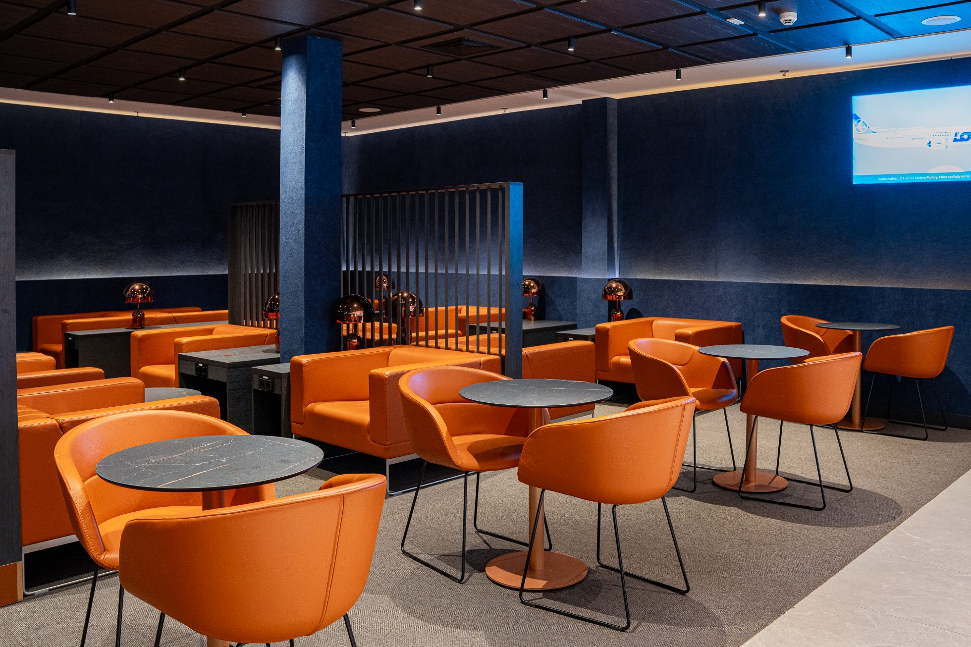 Elegancka przestrzeń z granatowymi ścianami i pomarańczowymi fotelami w Polonez Gold Lounge w Warszawie