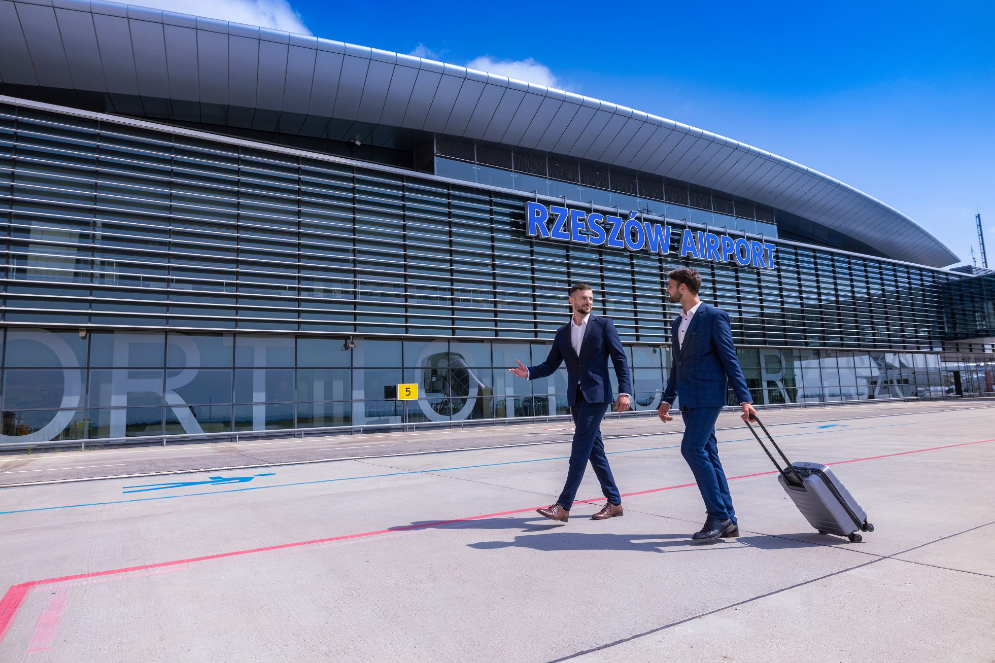 Zdjęcie budynku lotniska z nazwą Rzeszów airport z dwoma mężczyznami w tle 