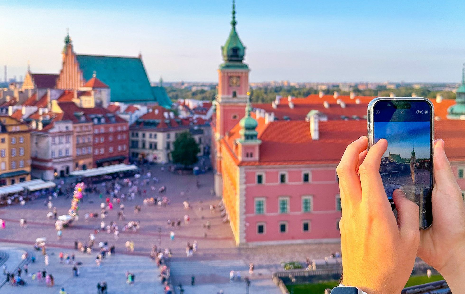 Mężczyzna trzymający telefon i robiący zdjęcie Starego Miasta w Warszawie.
