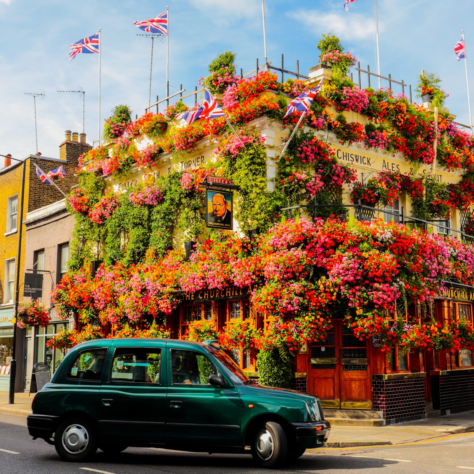 Budynek londyńskiego pub'u ozdobiony z każdej strony kwiatami i przejeżdżający zielony samochód obok, instagramowe miejsca w Londynie