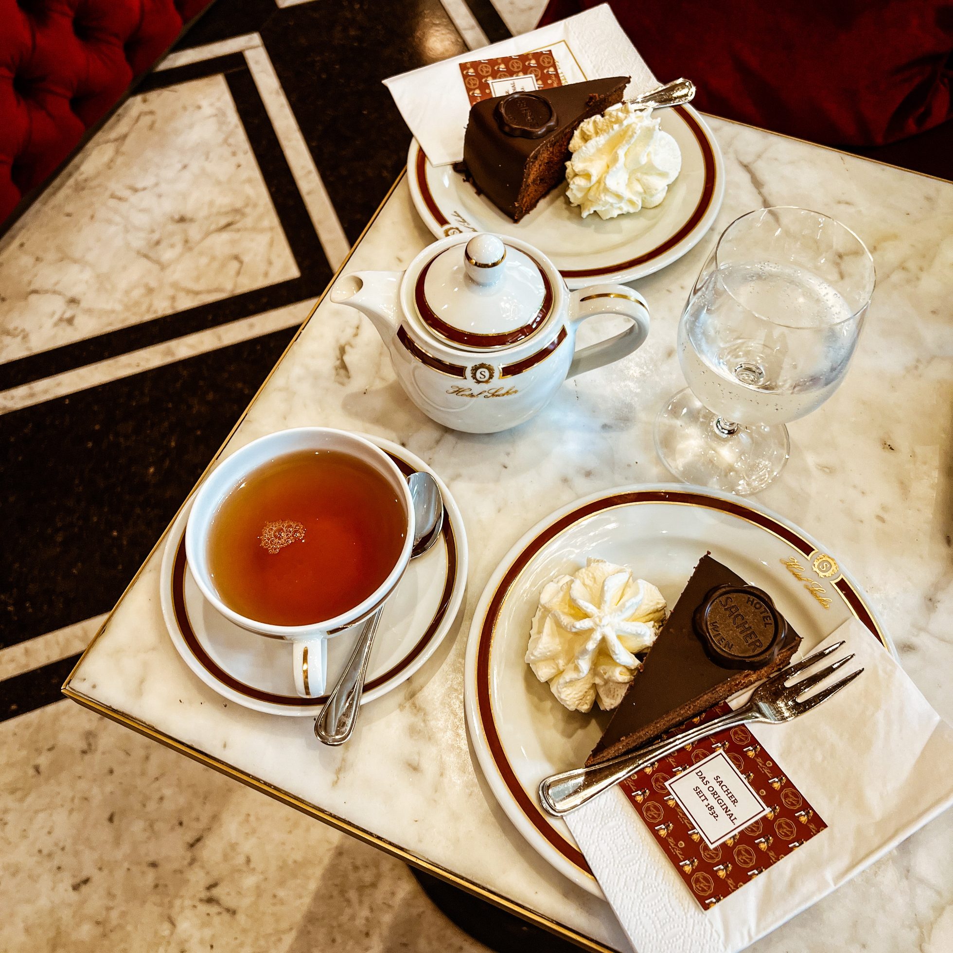 Czekoladowy Tort Sachera na eleganckiej zastawie porcelanowej, herbata w filiżankach. Wszystko postawione na marmurowym stoliku, kuchnia austriacka.