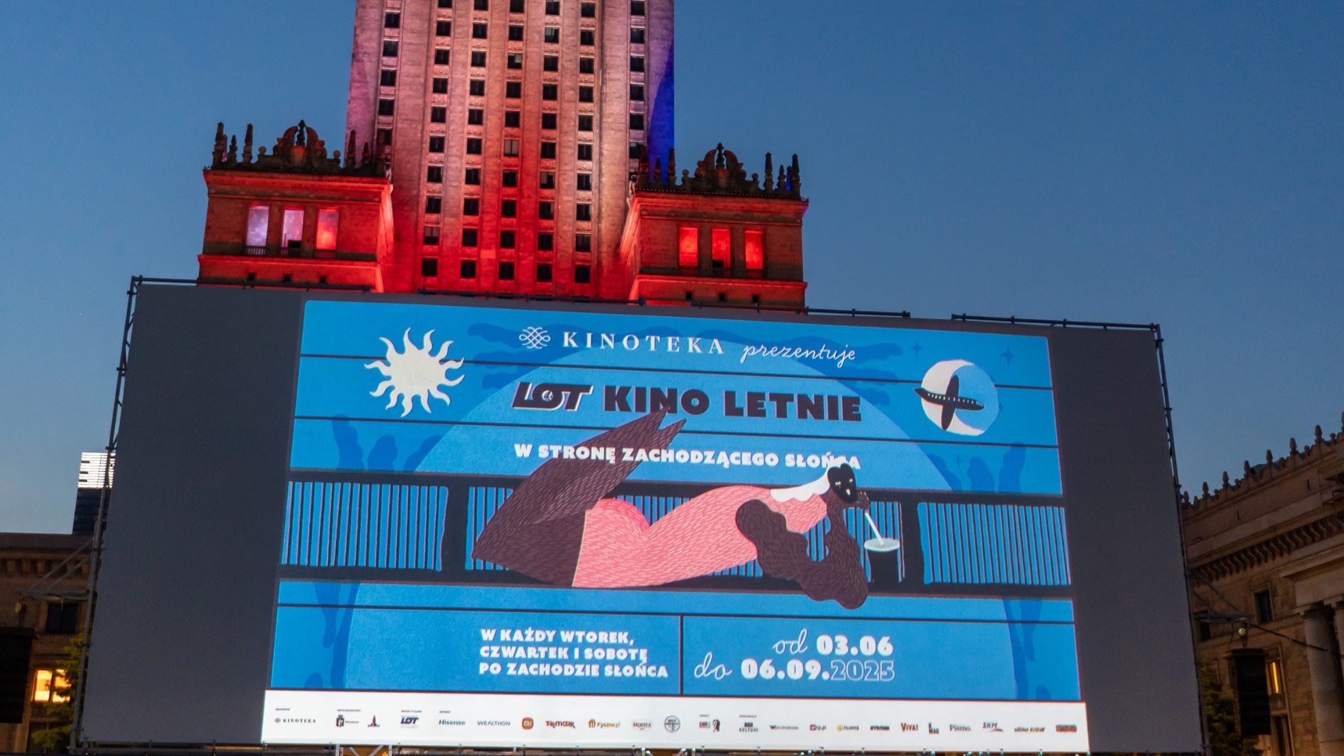 Big screen to show movies LOT Summer Cinema with the Palace of Culture and Science illuminated in red after sunset