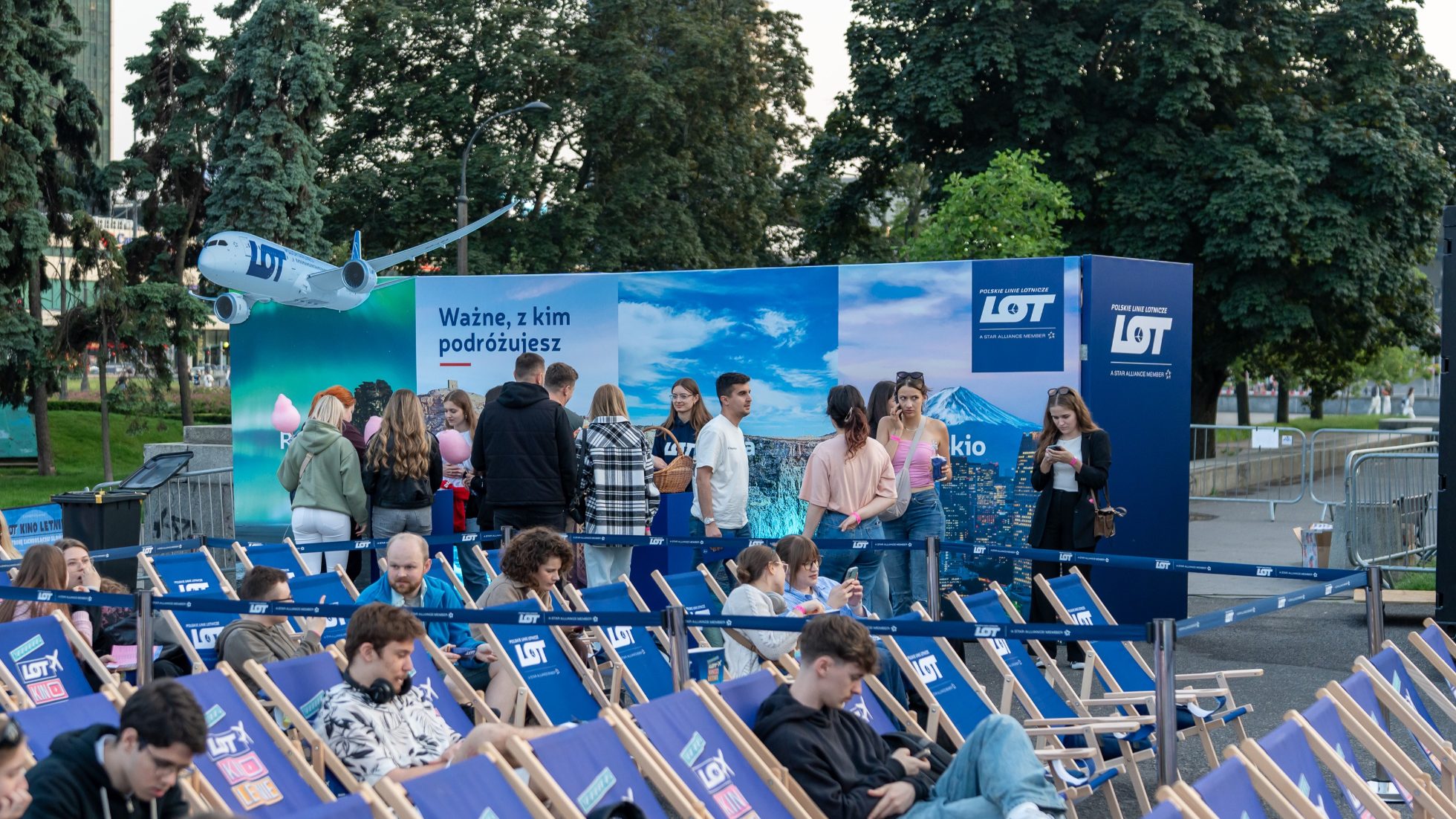 LOT summer cinema guests on deck chairs and LOT Polish Airlines promotional zone with LOT logo and Dreamliner plane in the background