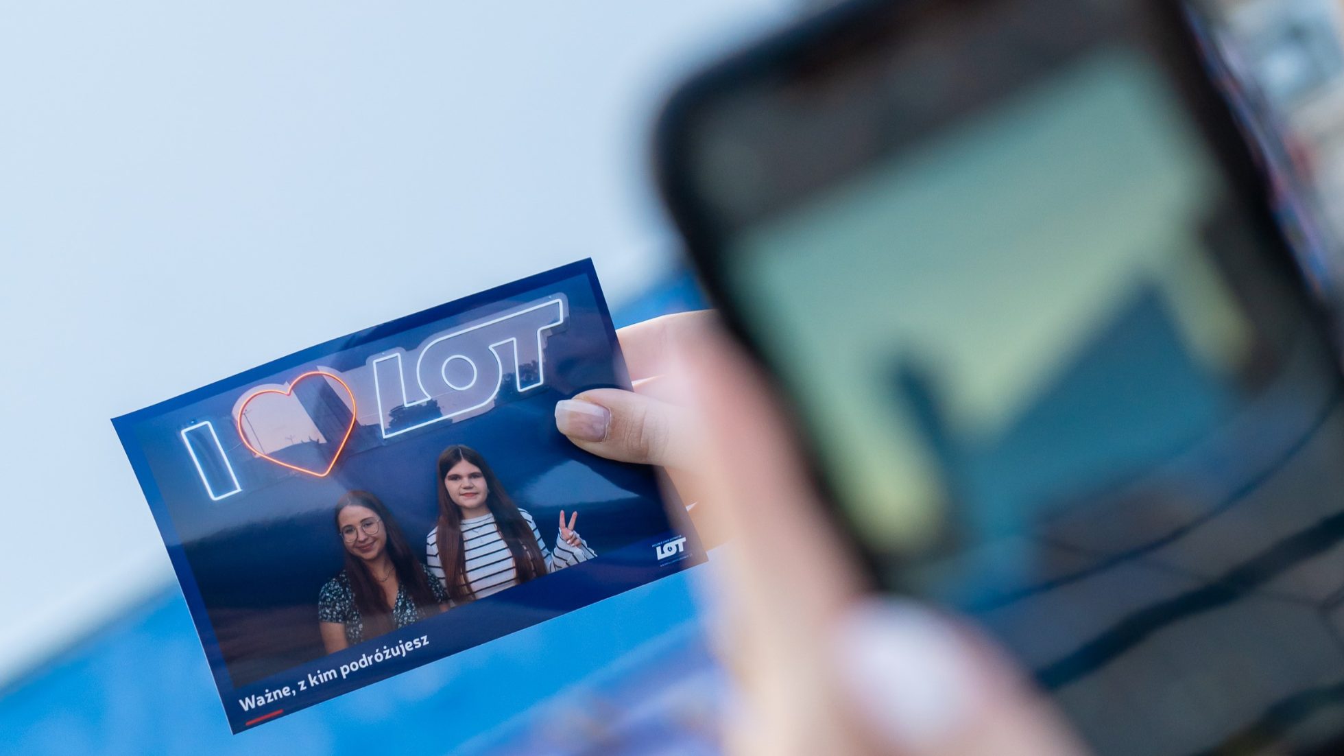 two women taking a picture of themselves on a wall with a neon I LOVE LOT sign