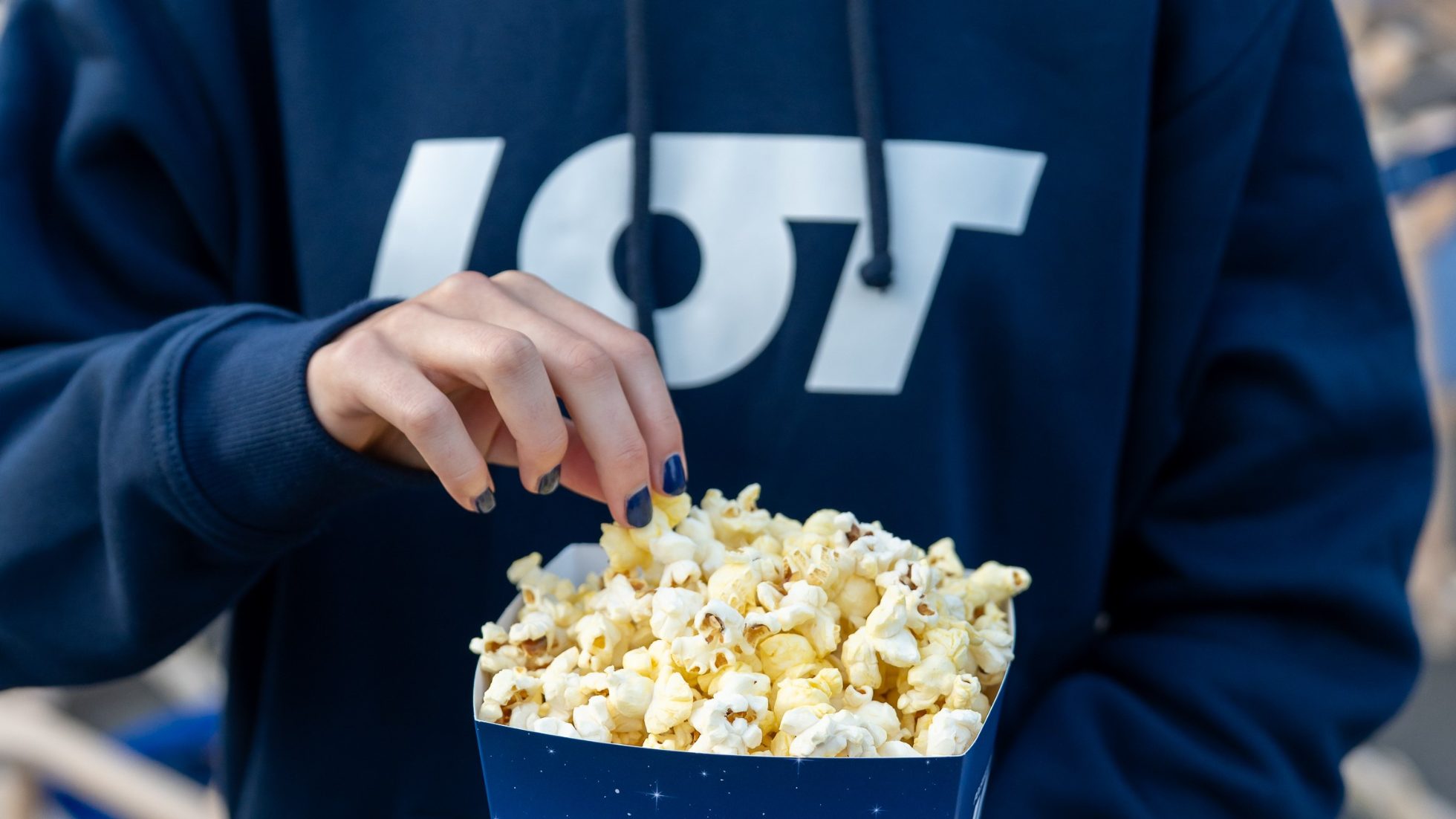 Girl wearing navy blue sweatshirt with white LOT lettering taking popcorn