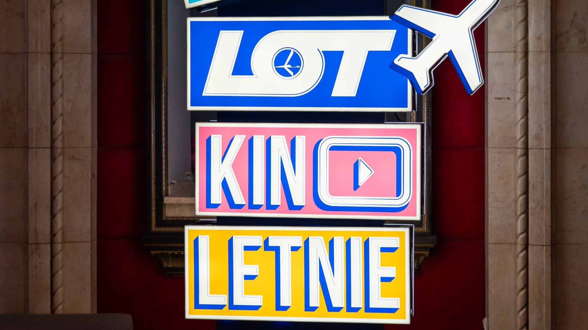Neon sign in blue, pink and yellow with the words LOT Summer Cinema and airplane
