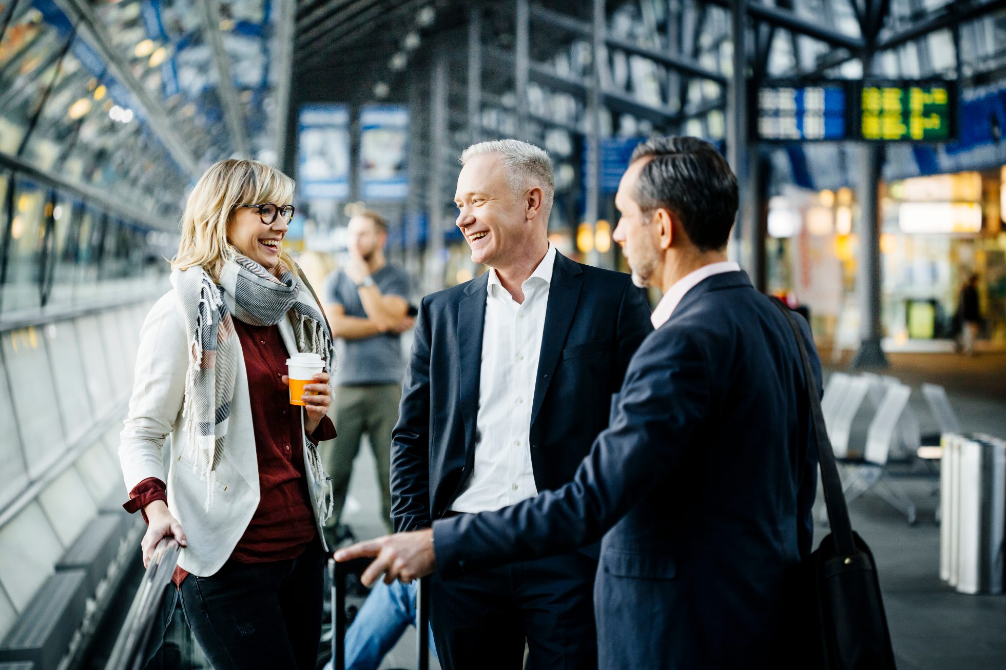 A trio of smiling business partners is chatting at the airport.
