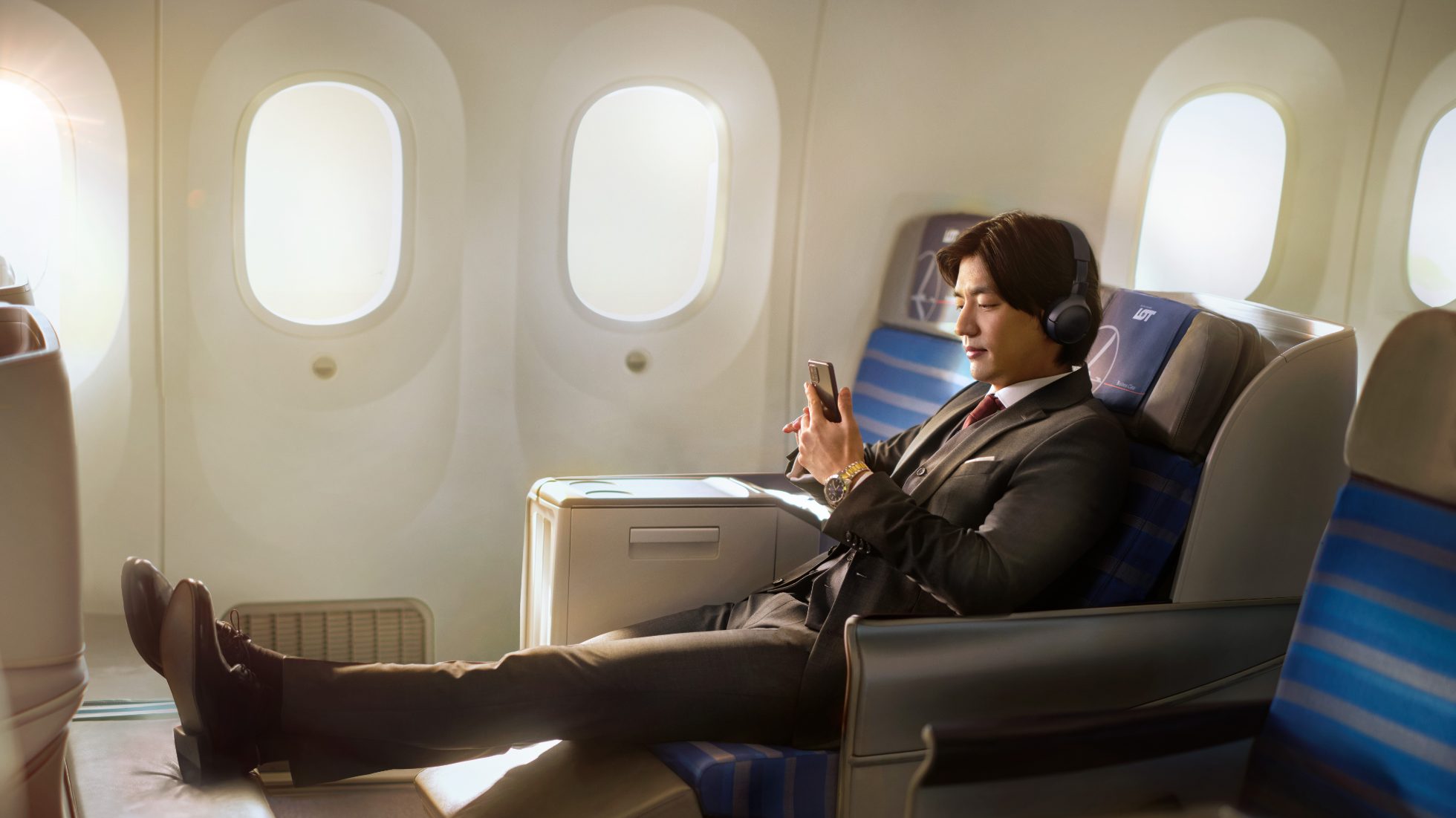 Person sitzt in einem Business-Class-Flugzeugsitz, hält eine Kaffeetasse und schaut aus dem Fenster.
