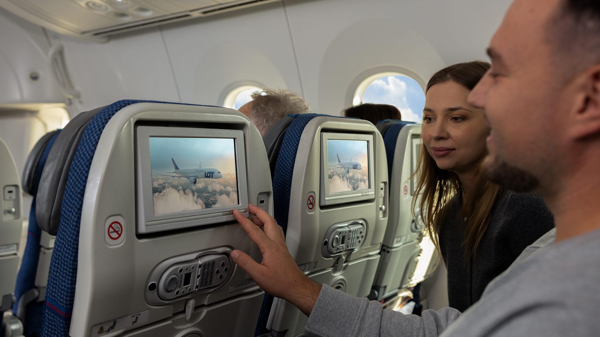 Passengers aboard Dreamliner, in Economy class check something on a screen mounted in the seat
